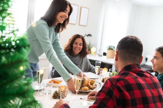 Happy caucasian young woman brings roasted chicken to table. Christmas family gathering. Holiday concept.