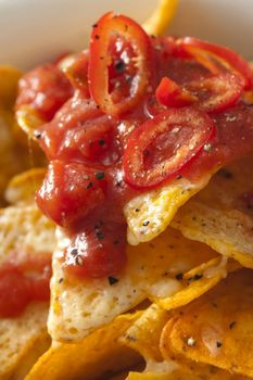 Topping of hot chili pepper and tomato salsa on corn tortilla chips with melted cheese for a tasty Tex-Mex or Mexican snack