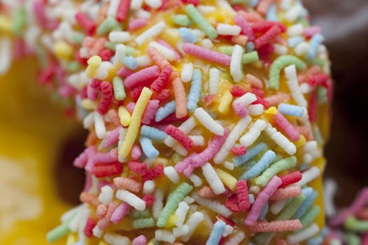Texture detail of colorful candy sprinkles on a fresh lemon glazed ring doughnut served for a morning coffee break