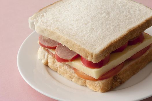 Tasty sandwich using plain white bread with cheese and sausage bits atop sliced tomatos