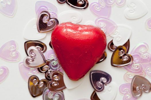 One red, chocolate valentine heart sits on top of a pile of smaller wedding heart decorations.