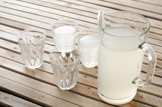 Fresh homemade lemonade in a jug sitting on wooden picnic table with two full and two empty glasses for a refreshing summer drink