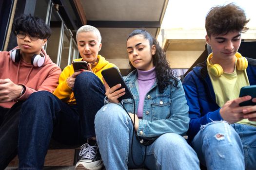 Group of teenage college friend students ignoring each other looking at mobile phone. Smartphone addiction. Youth lifestyle and social media concept.