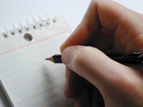 Man writing on a spiral bound notepad holding the pencil poised above the blank white ruled page, close up on his fingers