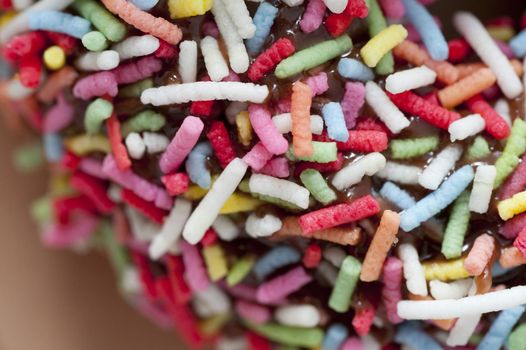 Background texture of multicolored sprinkles on a chocolate glazed doughnut