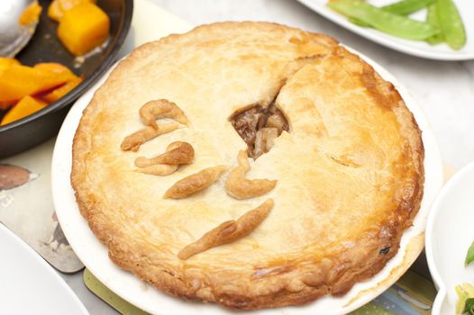 Tasty homemade meat pie with a golden pastry crust ready to be served with vegetables, close up high angle view