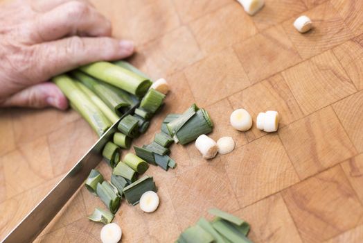 Man chopping fresh leeks for dinner with a large kitchen knife on a marble counter, with copy space