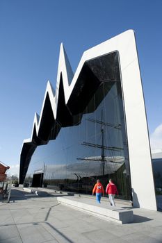 Distinctive modern exterior facade of the Riverside Museum, Glasgow. Scotland with its zigzag design and large window reflecting a tall ship in the harbour