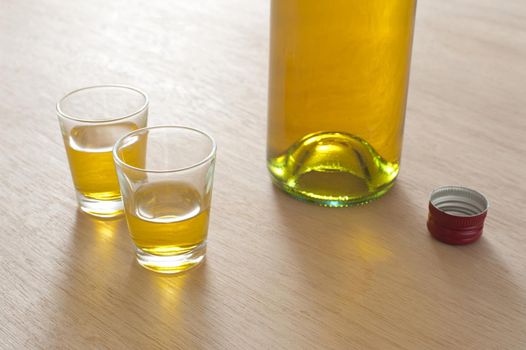 Two full shot glasses alongside a bottle of spirits, probably either whiskey or brandy, on a wooden bar counter