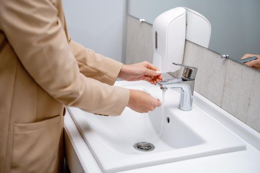 A woman washes her hands under running tap water in a public toilet