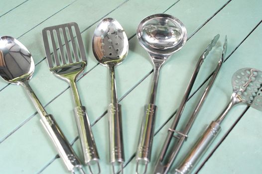 Set of clean stainless steel kitchen utensils displayed fanned out on a rustic green slatted table