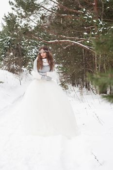 Beautiful bride in a white dress with a bouquet in a snow-covered winter forest. Portrait of the bride in nature.