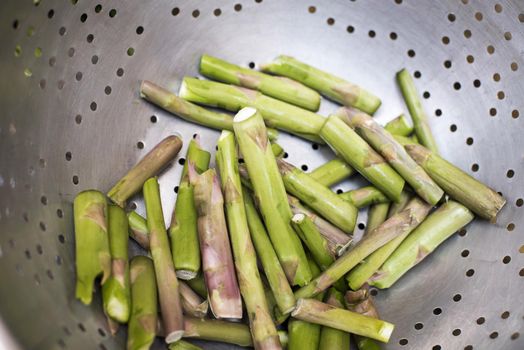 Cut asparagus stems in a metal colander, viewed in close-up. Preparing food process