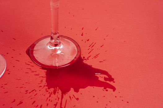 Red wine stain concept with a close up view of the stem and foot of a wineglass surrounded by spilt and splashed red wine on a red background with copyspace