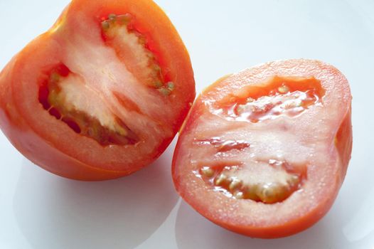 Halved fresh ripe tomato displayed to show the juicy pulp over a light grey background