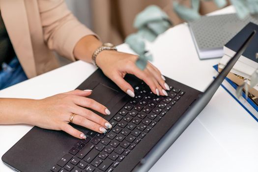 European professional woman sitting with laptop at home office desk, positive woman studying while working on PC. She is wearing a red plaid shirt and jeans