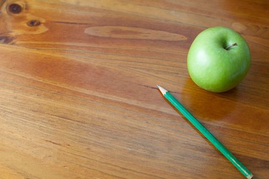 Schooled themed background of a wooden desk with a green apple and pencil