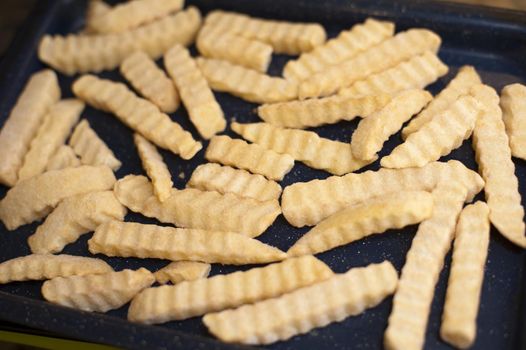 Frozen crinkle cut potato chips laid out on an oven tray for baking or cooking, close up view