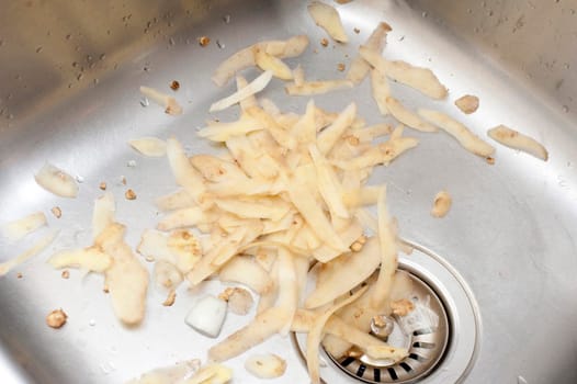 Potato peels lying in a stainless steel kitchen sink waiting to be discarded after preparing the vegetables for cooking