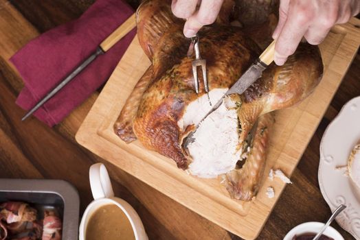 Man carving the breast of a Christmas turkey with vintage utensils in a cropped overhead view on the table