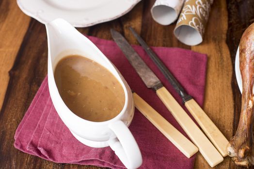 Turkey gravy in a white sauce boat on a Christmas table with a vintage bone handled carving set and crackers