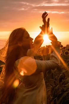 Beautiful middle aged woman looks good in a hat enjoying nature in a field of sunflowers at sunset. Summer. Attractive brunette with long healthy hair