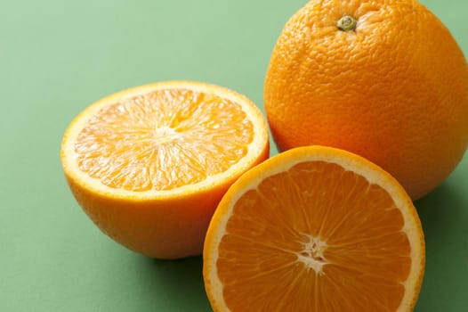 Whole and halved juicy fresh orange over a green background in a healthy diet and nutrition concept