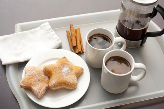 Plunger coffee with two mugs of freshly brewed coffee served on a tray with cinnamon sticks and star-shaped biscuits on a plate