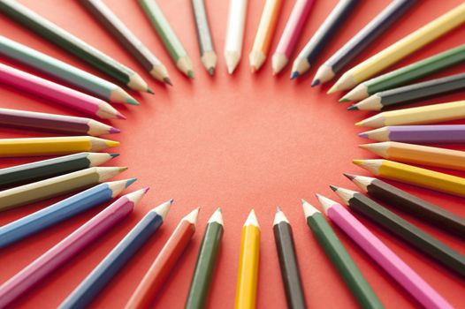 Circle shape formed by various multicolored sharp colored pencils over red background