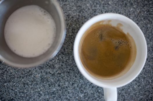 Close-up of two glasses, one with espresso, other with cream, standing on table.