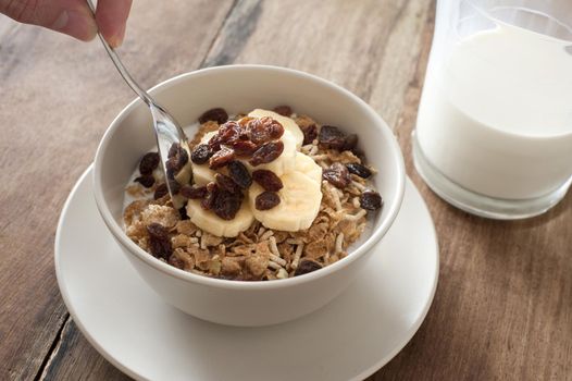 Eating healthy muesli topped with fresh sliced bananas and raisins for breakfast with a jug of milk to the side