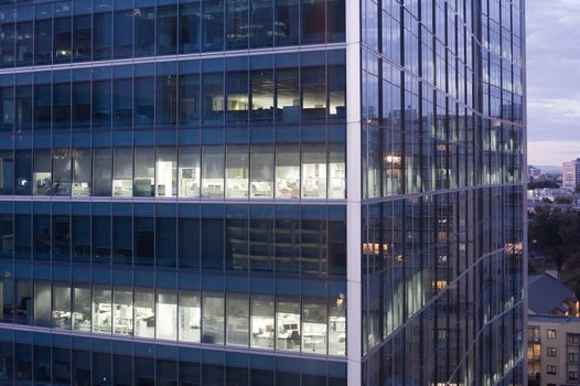 Modern skyscraper office block at night with interior lights illuminated showing office furniture and layout