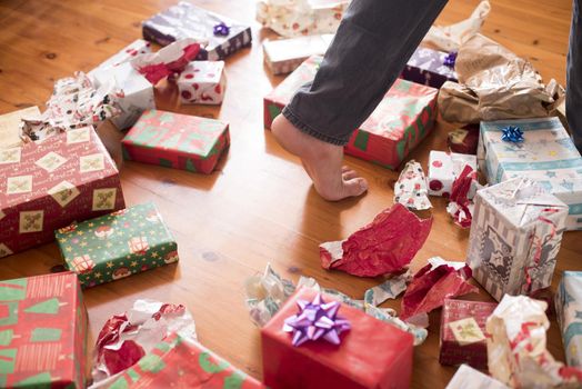 Christmas day concept with a bunch of gift boxes on the floor at home and a person foot stepping over it