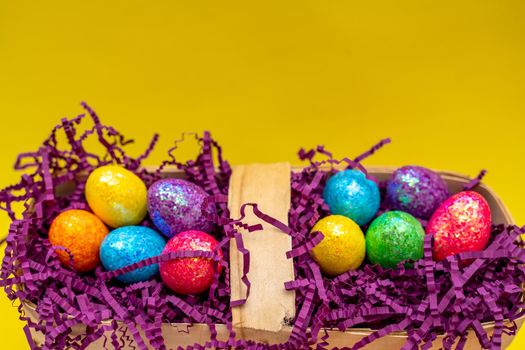 Easter composition from a basket and colored eggs prepared for the holiday on a yellow background.