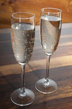 Two full flutes of champagne or sparkling white wine standing side by side on a wooden counter conceptual of a romantic evening or celebration