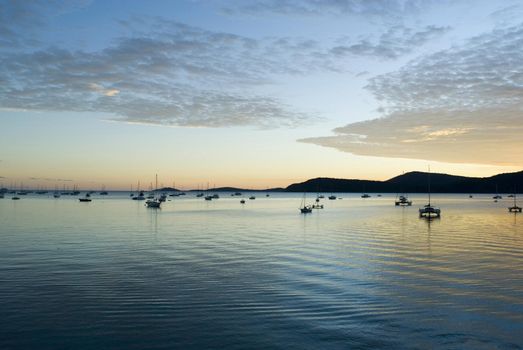 serenity of a still sunset over the water, yachts moored as the sun dissappears below the horizon