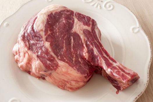 A close up of a raw rib eye steak on a white, porcelain plate.