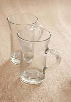 Two empty clean tea glasses with handles side by side on a wooden table