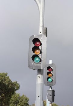 A set of street traffic lights in portrait orientation against a stormy overcast sky.