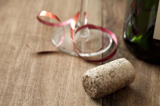 Party copy space with glass tied with a red ribbon, cork and bottle over a wooden background with copy space