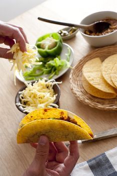 Man preparing corn tortillas adding grated cheese, fresh green bell pepper and minced savory beef