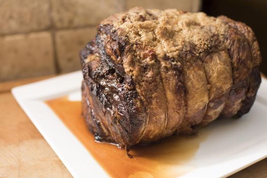 Whole trussed seasoned roasted beef joint served on a plate with meat juice in a close up side view