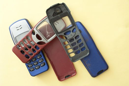 Old loose red, black and blue covers for mobile phones with a button design, one with a cracked screen on a yellow background