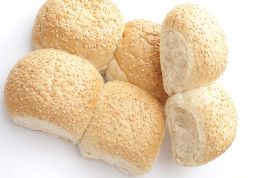 Batch of fresh joined sesame rolls from a bakery with two broken off to show the texture of the bread viewed overhead on white