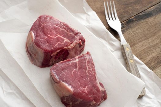 Two juicy thick tender raw medallions of beef fillet steak on greaseproof paper waiting to be prepared for dinner