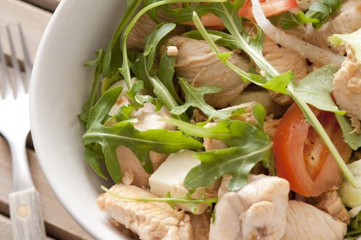 A close up of a healthy chicken salad dish with rocket on a table with fork.