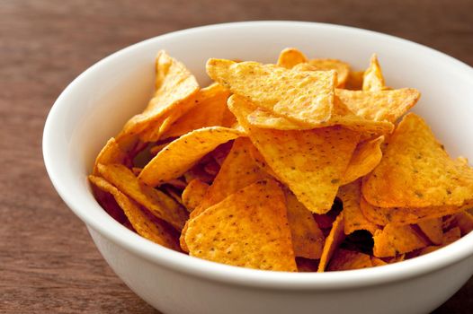 White round bowl full of yellow corn tortilla chips over dark brown wooden table