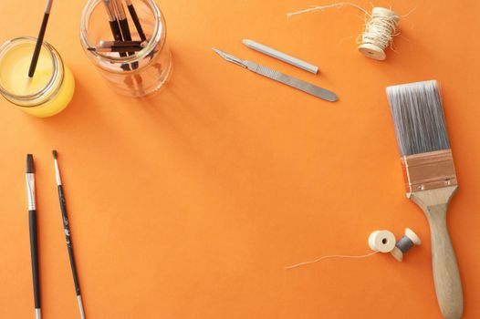 High Angle Still Life of Various Art Supplies and Paintbrushes Scattered on Orange Surface with Copy Space in Center of Page