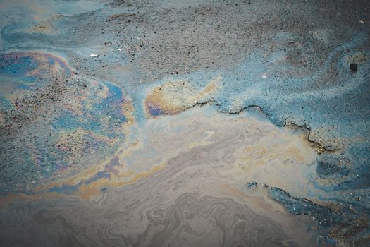 Multi-colored poisonous spots of spilled gasoline on wet asphalt. Environmental pollution concept