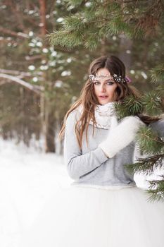 Beautiful bride in a white dress with a bouquet in a snow-covered winter forest. Portrait of the bride in nature.